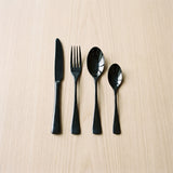 Greece Set — glossy black flatware on a warm wood table